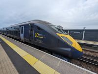 Dark blue train with long and thin yellow nose sits in a platform. The sign in the background reads Thanet Parkway.